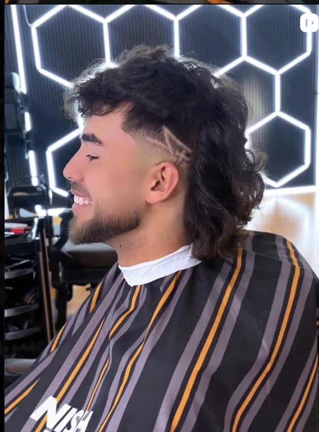 Modern mullet with a razored side design, cut in front of the glowing hexagon wall at Z Barbers